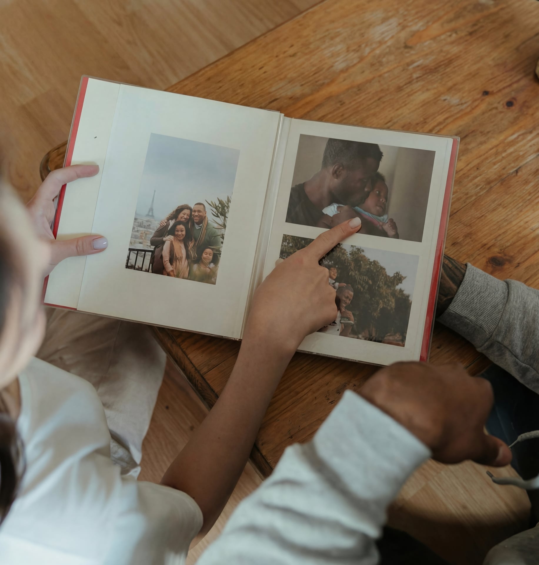 To personer ser på et fotoalbum sammen ved et trebord, peker på familieminner